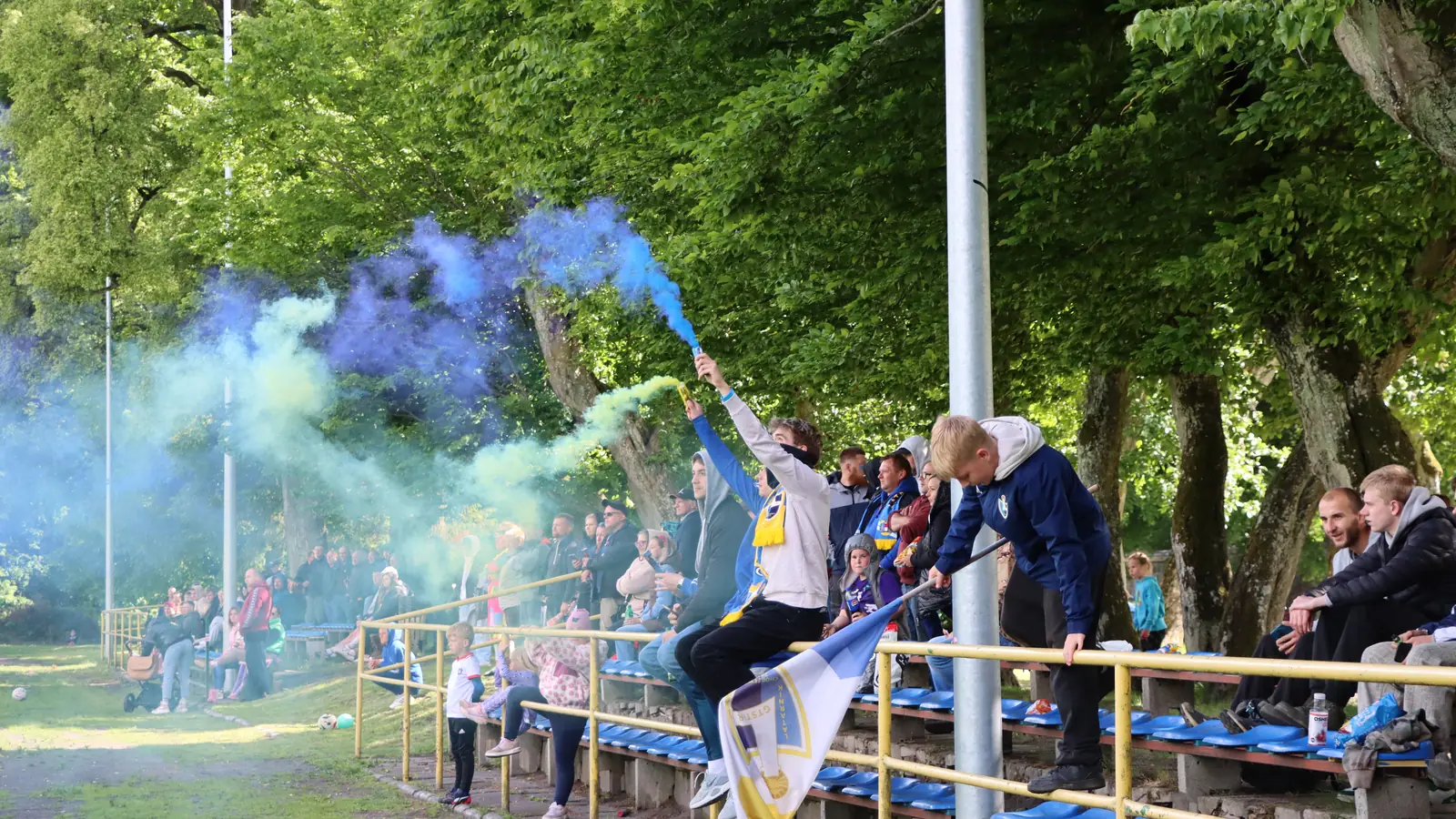 Kibice Latarnika na trybunie w Choczewie, z flagą klubu i dymem w barwach niebiesko-żółtych
